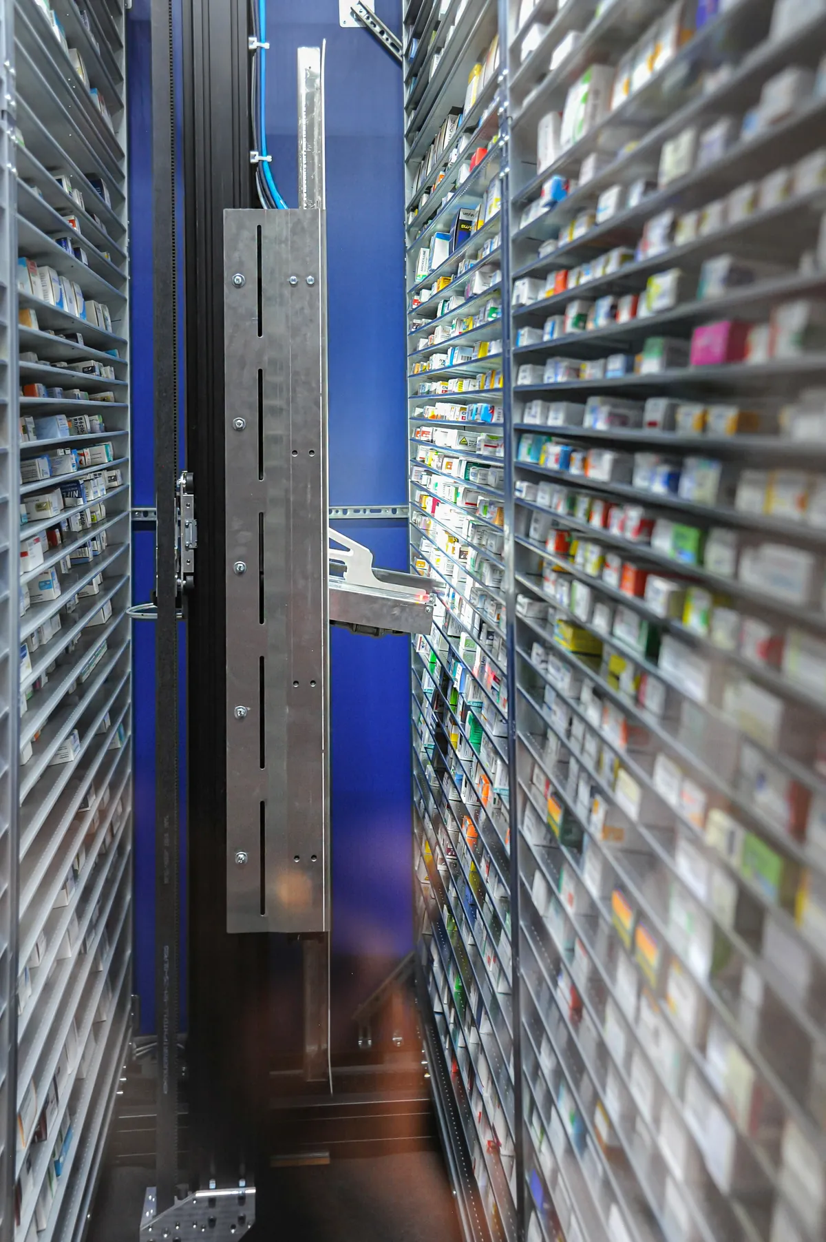 Corredor interno do robô Gollmann, com a garra entre duas estantes altas cheias de embalagens de medicamentos.